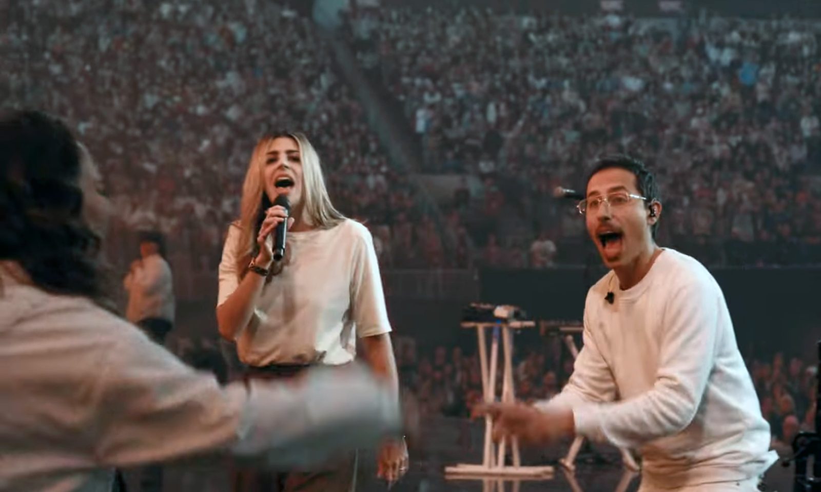 Robby directing a choir on stage behind Brooke Ligertwood at a Passion event